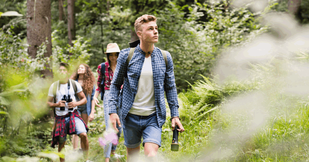 Four young people hiking, showing youth leadership in a lush, green forest by day.
