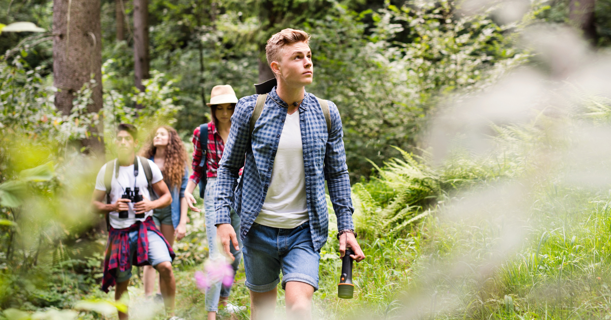 Four young people hiking, showing youth leadership in a lush, green forest by day.