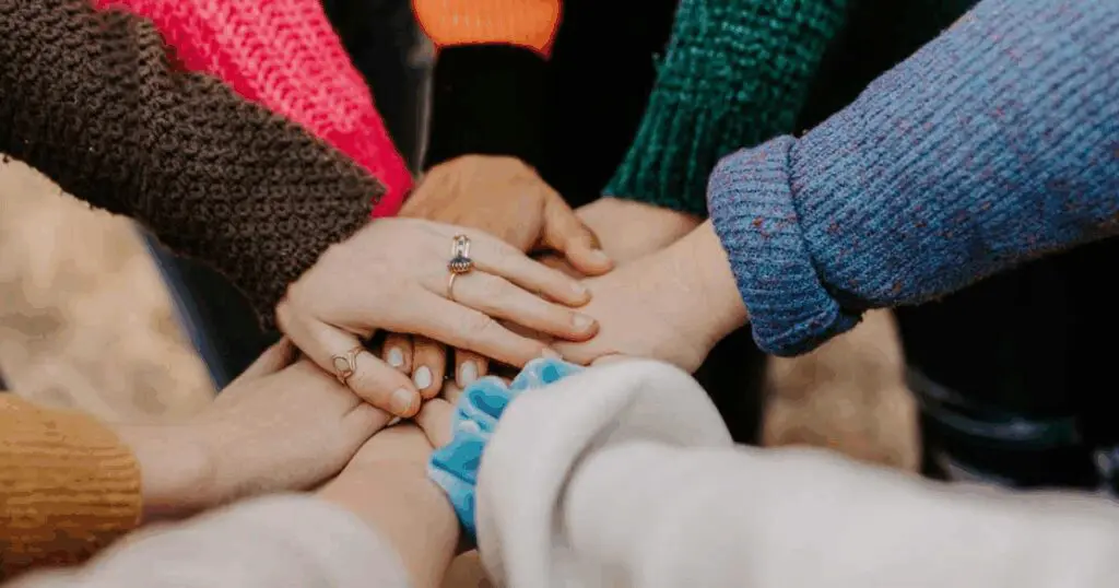 A group of people stacking their hands together in a show of unity and ground up teamwork.