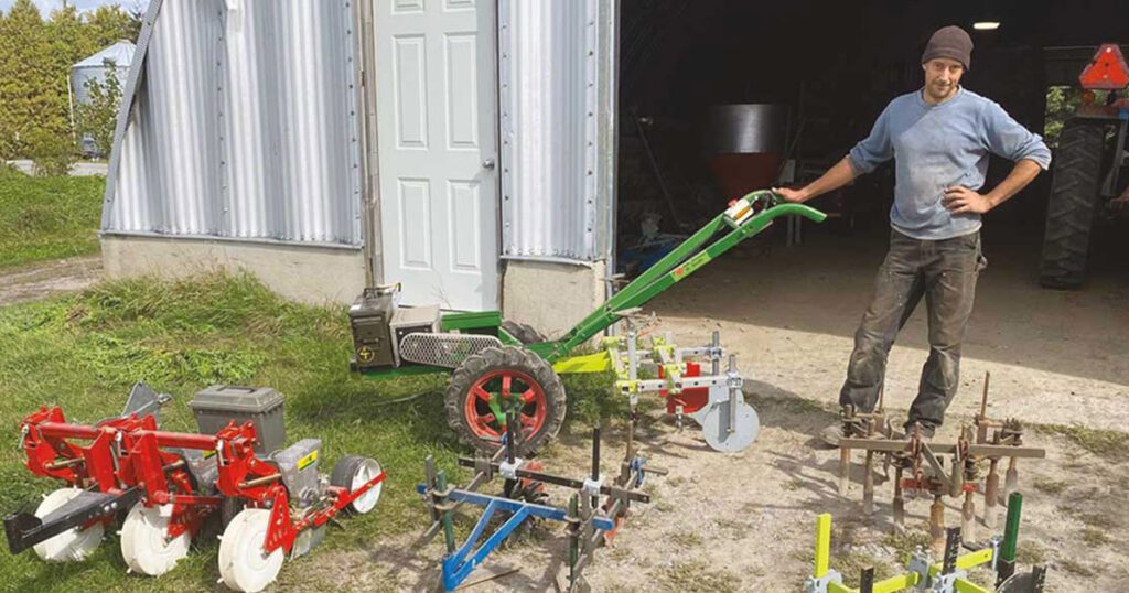 A young man stands among a selection of two-wheel tractors.