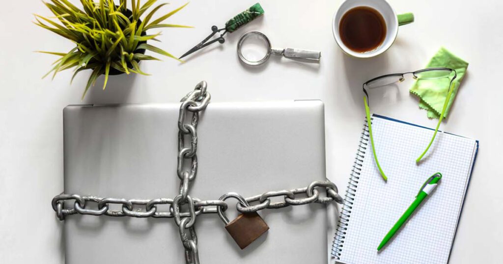 An overhead view of a cup of coffee, a pad of paper, and a laptop that is wrapped with a chain and lock