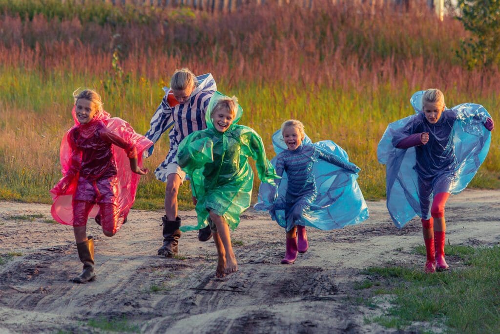 A group of kids in rain ponchos running outside