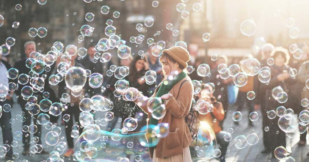 A woman plays with giant bubbles while a crowd looks on