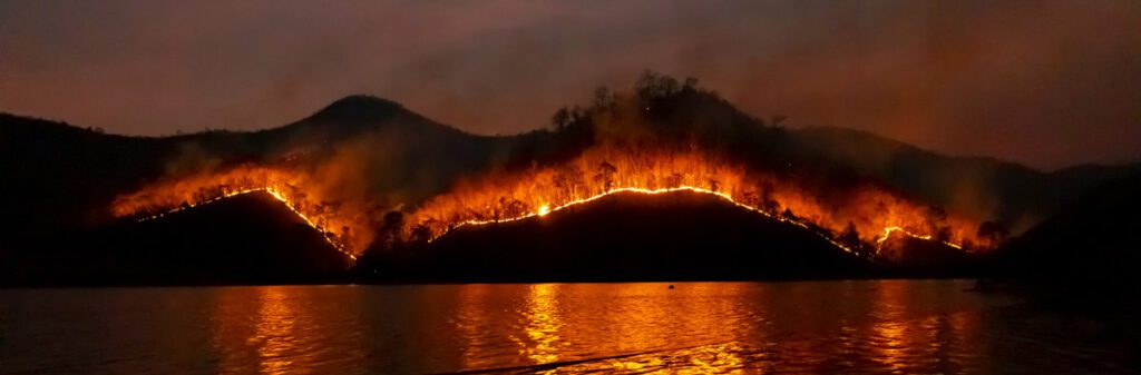 A mountain side on fire across a lake