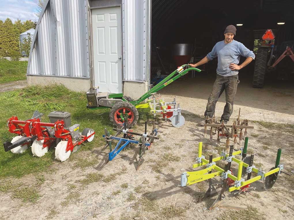 A young man stands with a selection of two-wheel tractors.
