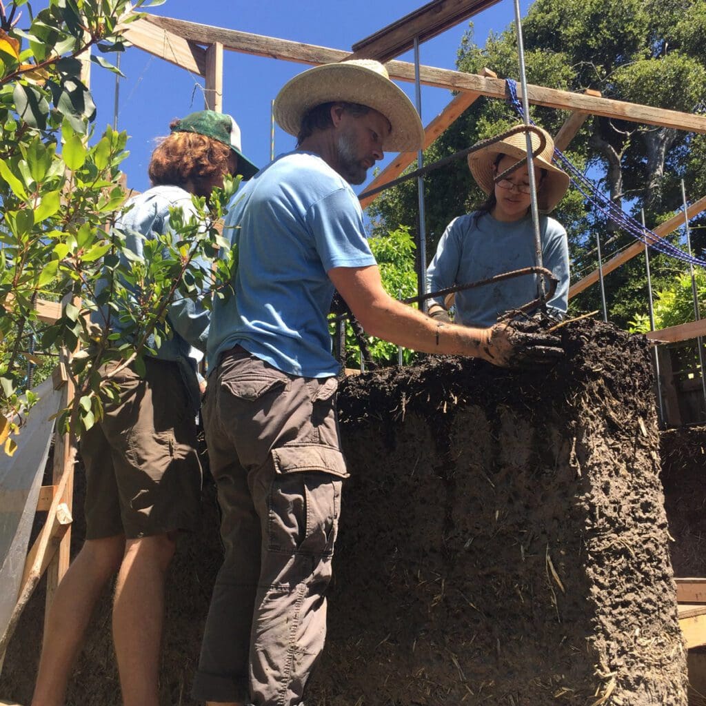 A group of workers build the mud and clay walls of a home.