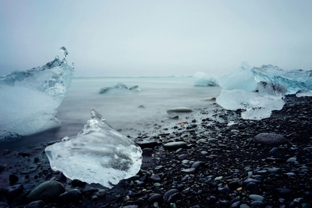Large chunks of ice surround the pebbled shore of the ocean.