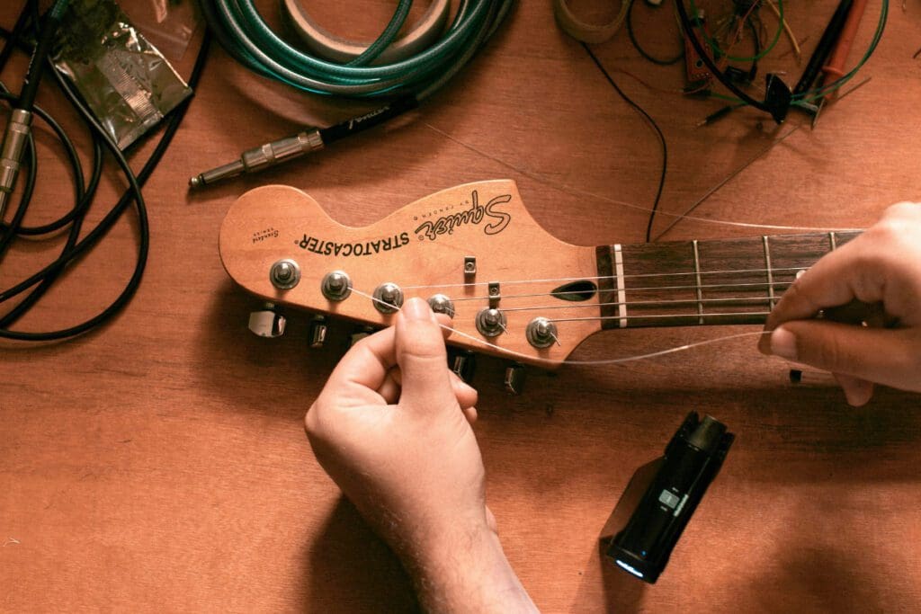 Hands replace the strings of a guitar on a wooden table.