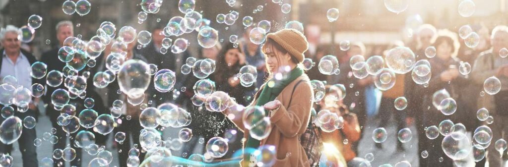 A woman plays with giant bubbles on a city street while onlookers watch.