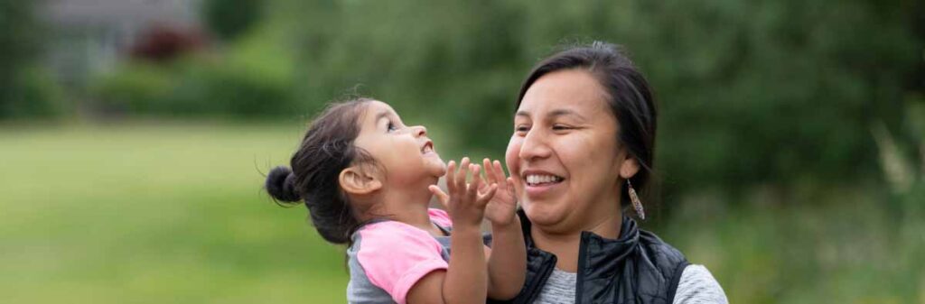 Young, smiling woman plays with a young child on the grass.