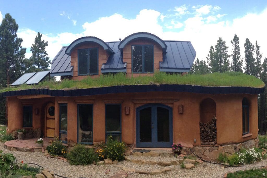 An orange clay home with a grass roof, patio stones and pebbles/shrubs for landscaping.