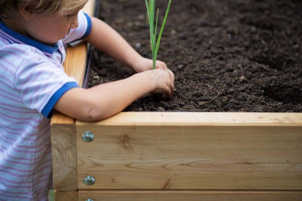A young boy planting in a large  garden box.