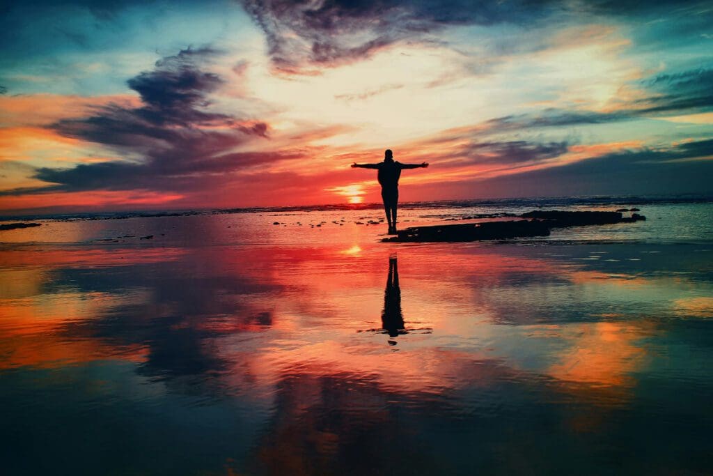 A silhouette of a person with their arms out on a beach at sunset