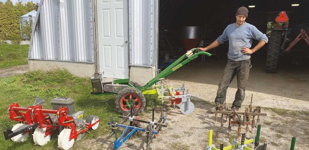 A young man stands among a selection of two-wheel tractors.