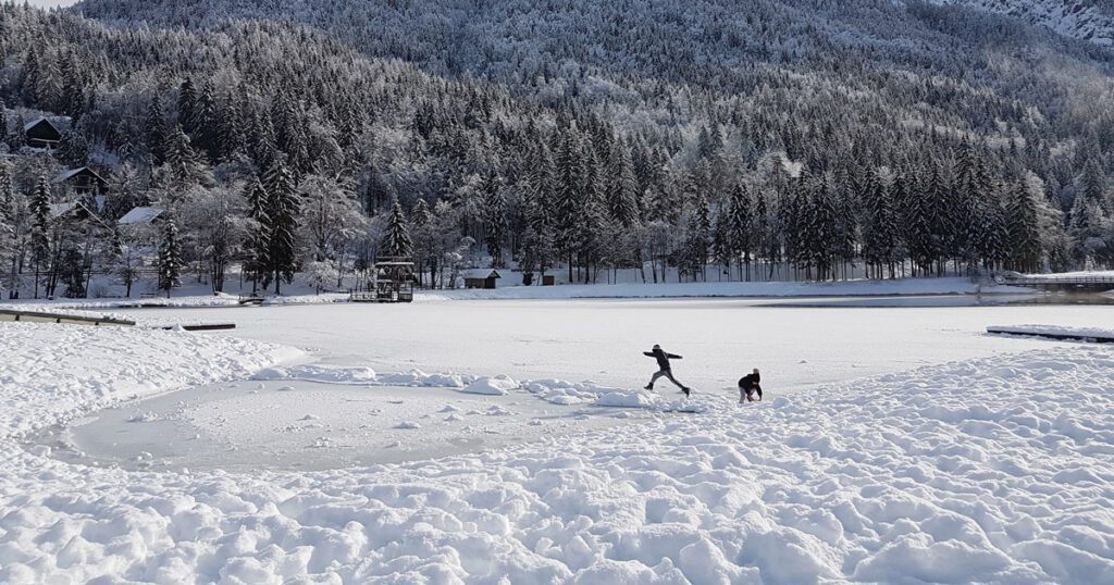 Two children playing on an ice-covered lake in the winter.