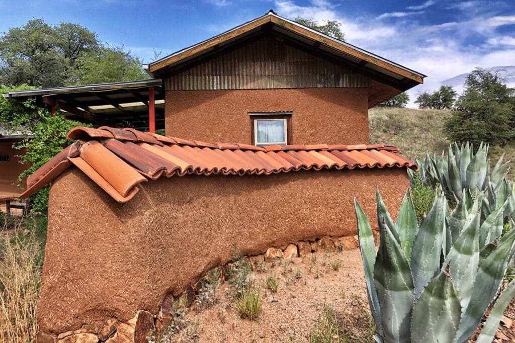The side view of a clay home with a log and clay back fence.