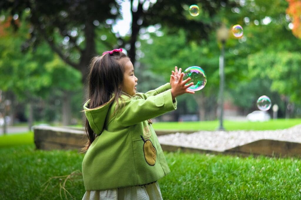 Young girl chases big bubbles in the park.