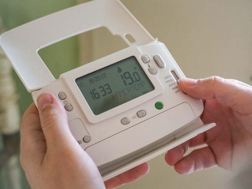 Hands holding a digital thermostat showing a 19 degree temperature.
