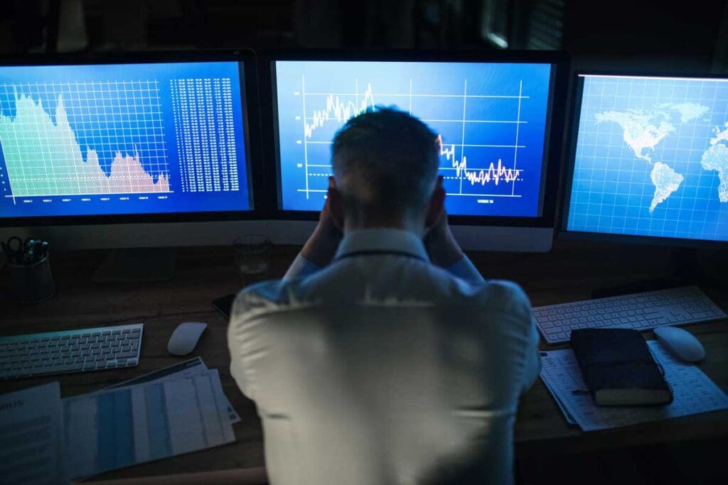A man sits at a row of computer screens showing graphs and maps.