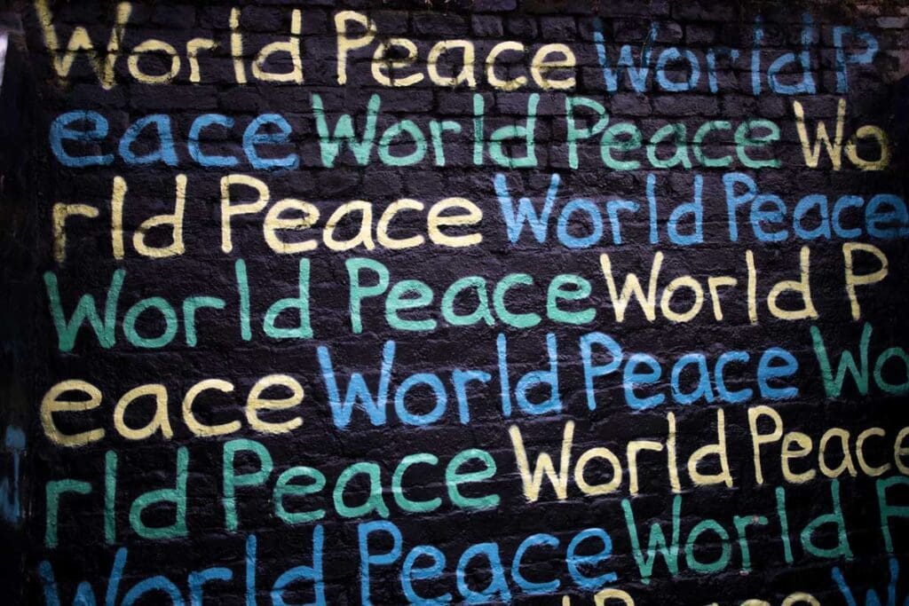 World Peace is spray painted multiple times in yellow, blue, and green on a black brick wall.
