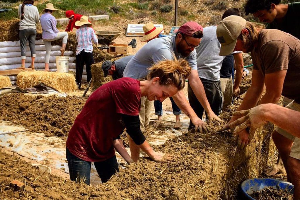 A group of people work together to form the sand and straw walls of a cob home.