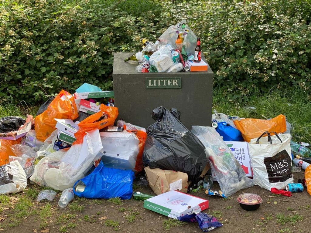 Plastic bags overflow with litter on the ground in front of bushes.