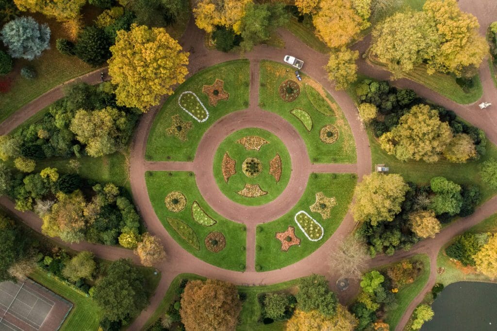 Grassy circular clearing with plants and surrounded by walking paths amongst trees. A truck sits near the top.