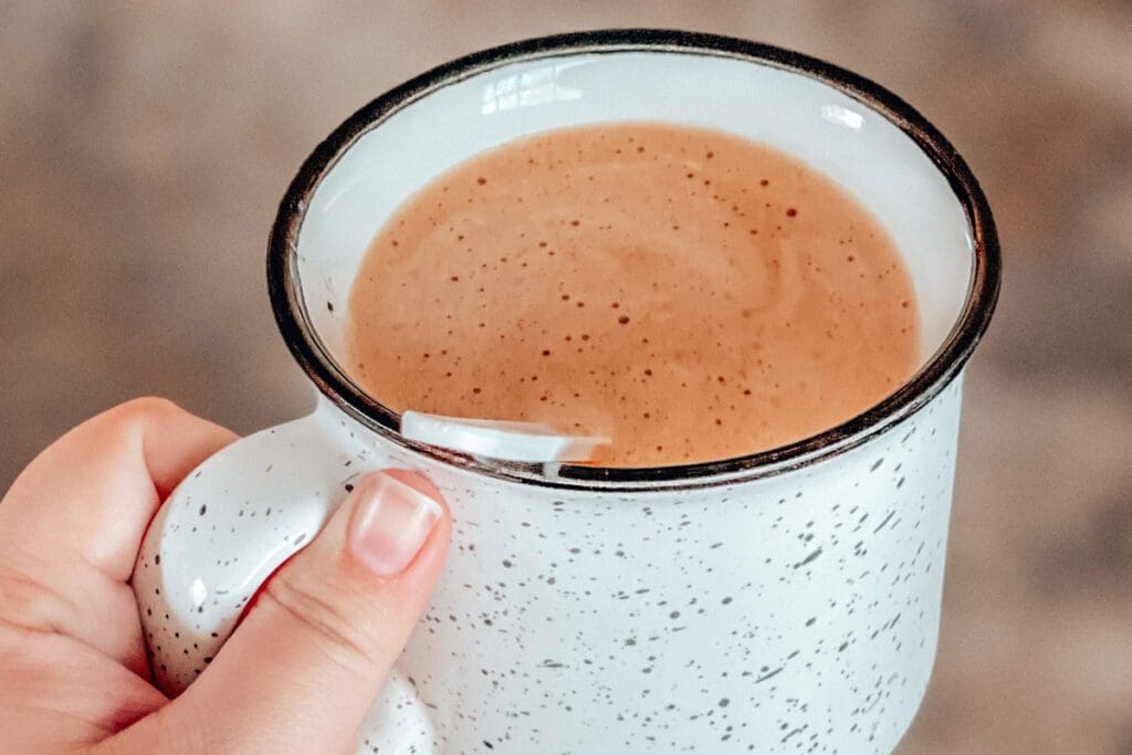 Hand holding a cup of hot cocoa with a plastic spoon.