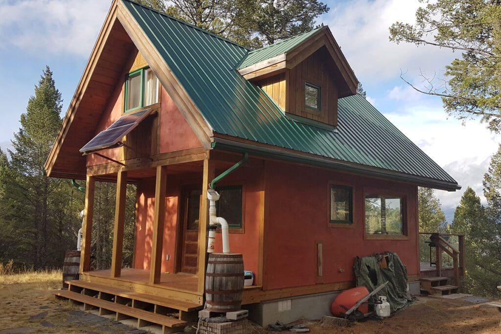 2-story rural cottage with a front and back deck, solar panels and a rainwater harvesting barel set up on the side of the front porch.