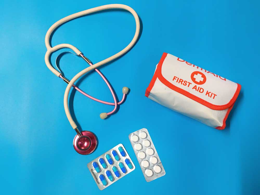 A small first aid kit, two pill packets and a stethoscope on a blue background.