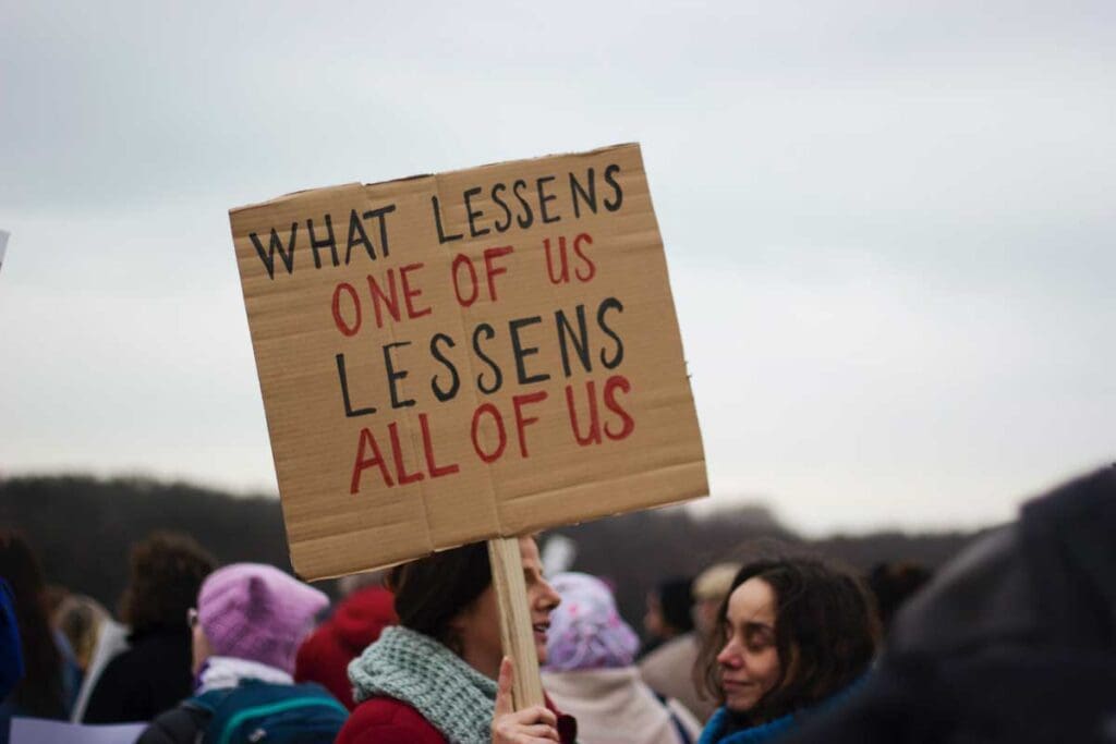 Protesters holding a sign reading: What lessens one of us lessons all of us.