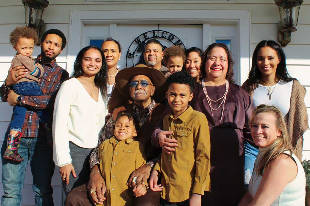 A large multi-generational family stands in front of the door to a house.