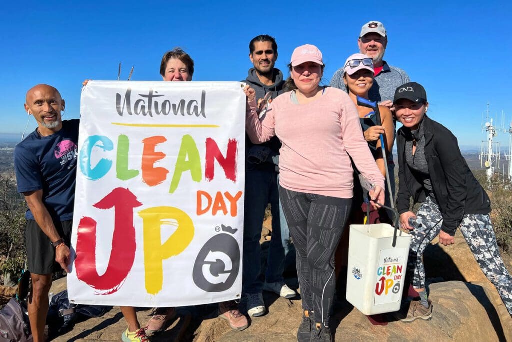A group of volunteers pose on a rock for a photo Holding a banner for National Clean Up Day.