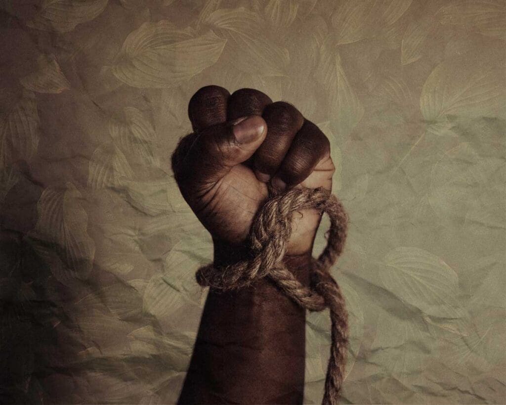 A close-up of the clenched fist and arm of man with a rope knotted loosely around the wrist.