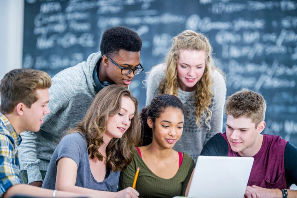 A group of students looking at a laptop with a filled chalkboard in the background