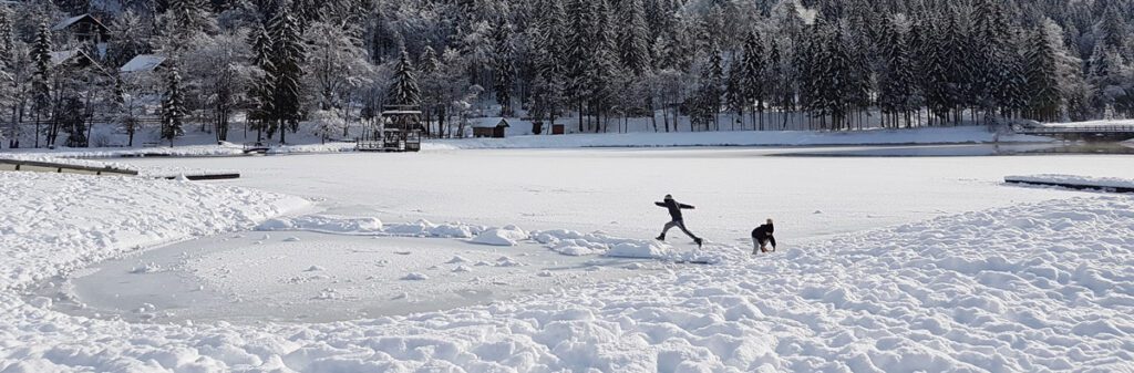 Two kids playing on a frozen lake in winter.