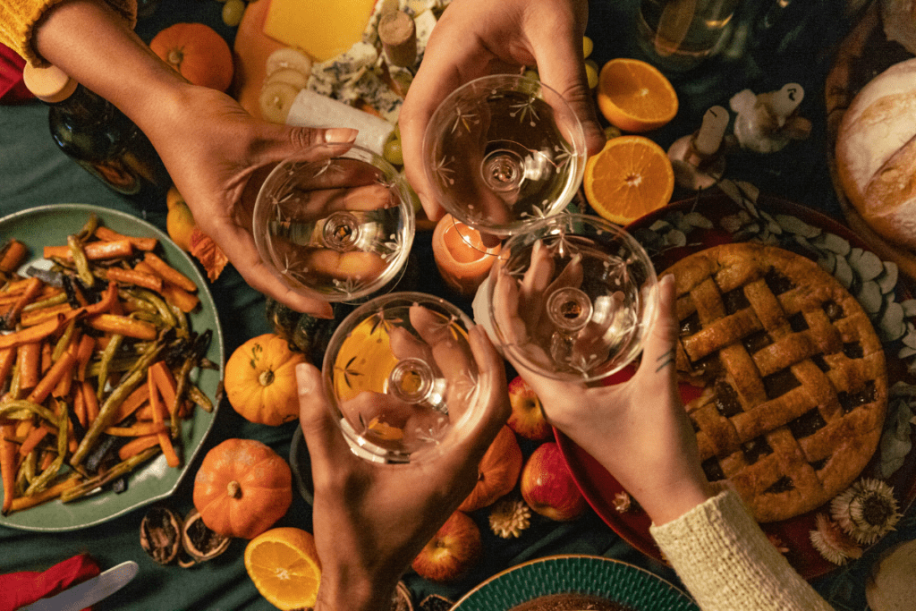 Four people are raising their glasses in a toast over a beautifully decorated table, which is adorned with plates of vegetables, pie, and fruits.