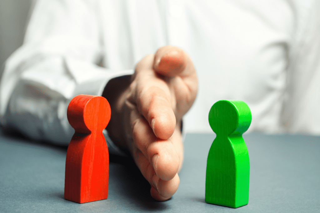 A man’s hand sits between a green and red wooden person.
