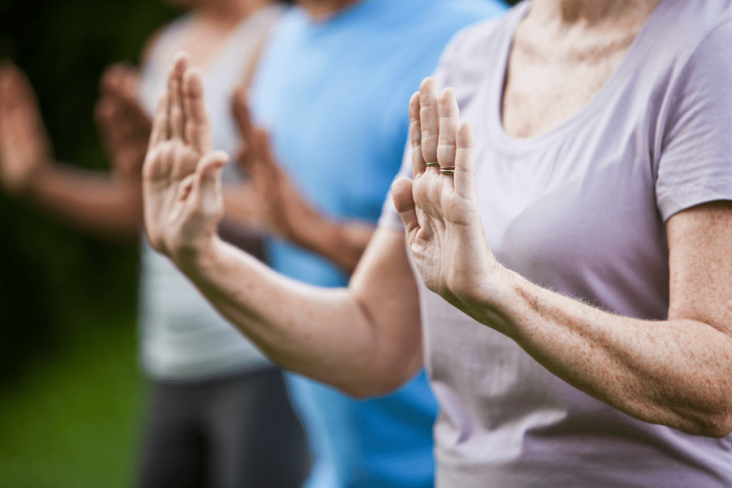 In a group, an older woman holds her hands out on front of her in a tai chi move.