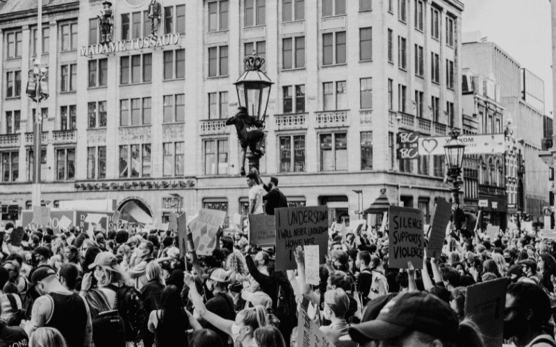 A black-and-white image of protesters march along the streets in front of a building with the name "Madame Tussaud"
