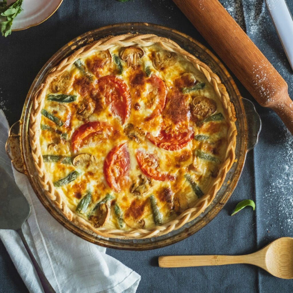 A homemade pizza with cheese, tomatoes, mushrooms, and green peppers next to a rolling pin.