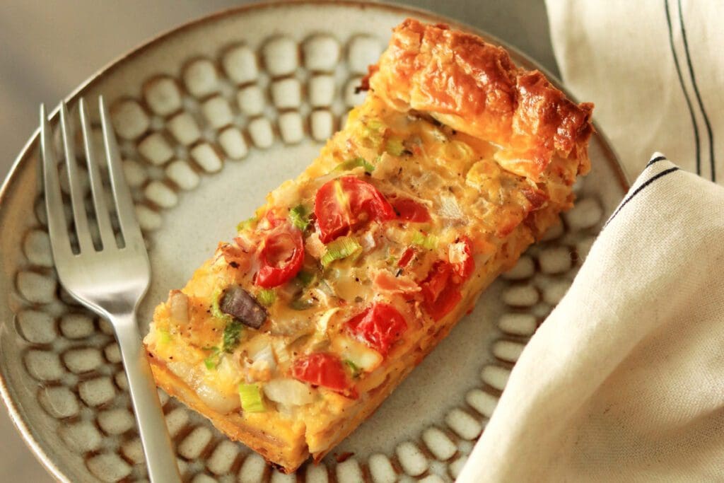 A slice of freshly baked quiche with tomatoes on a plate.