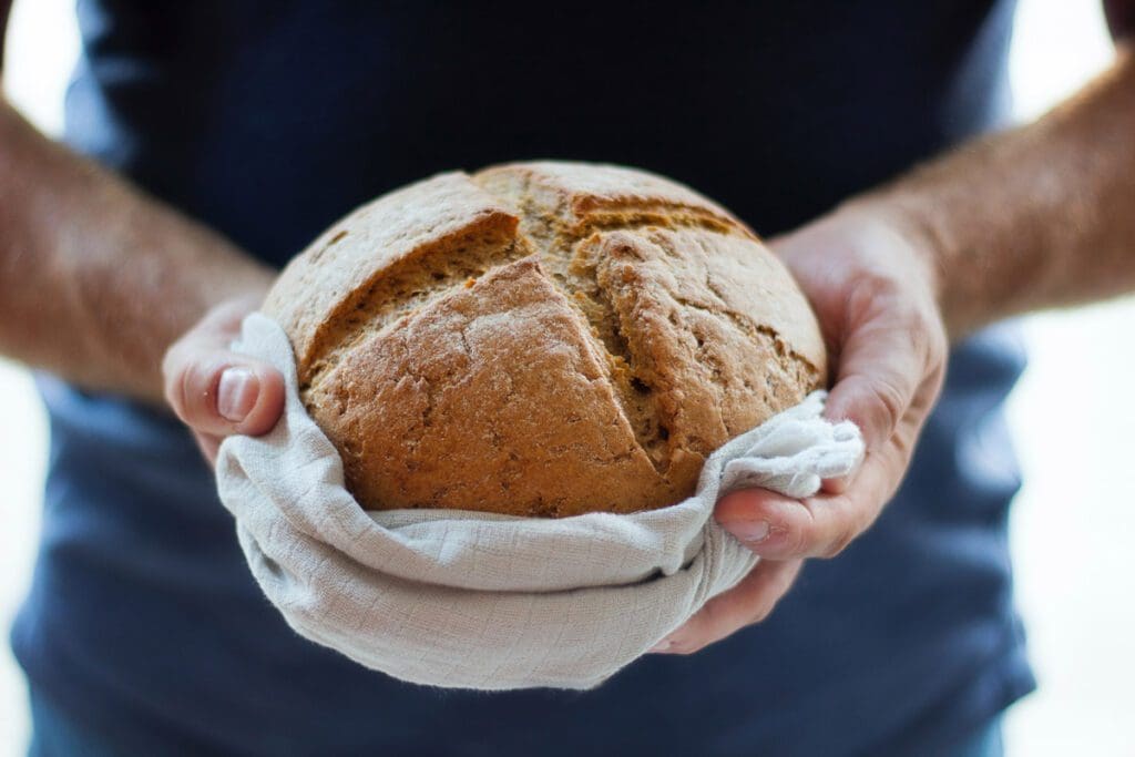 Hands hold a freshly baked loaf of bread in a linen cloth.