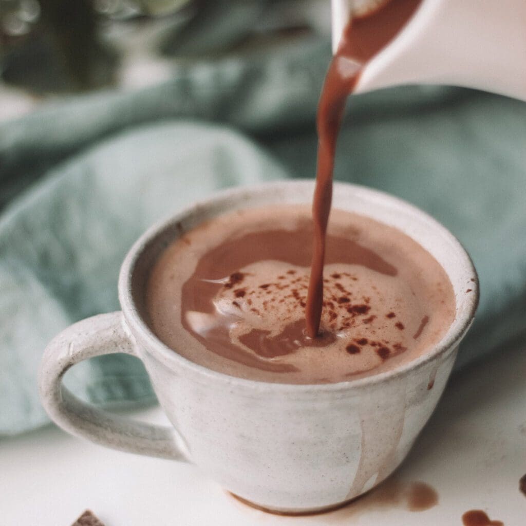 Hot cocoa splashes the outside of a white mug as it is poured.