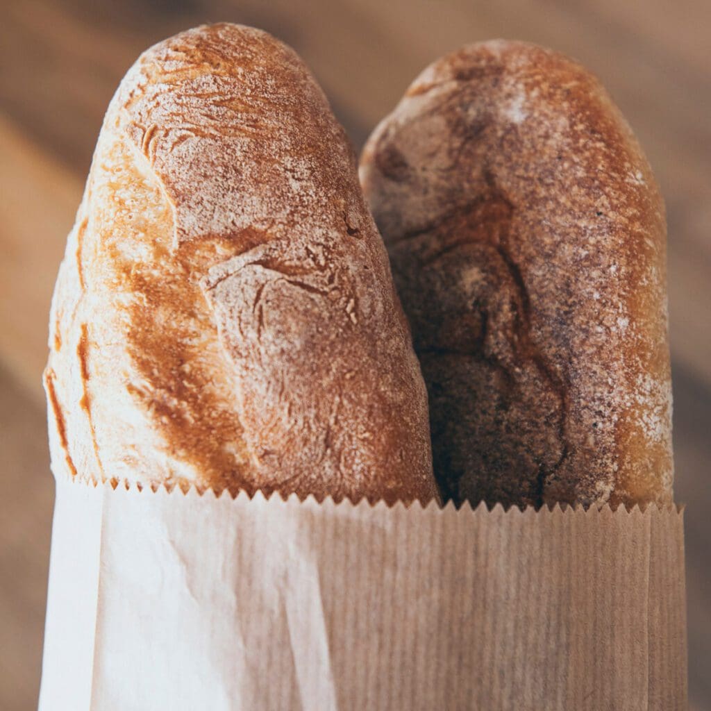 Two loaves of fresh baked bread in a  paper bag.