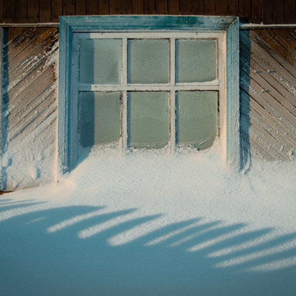 A snow drift reaches halfway up the window of a house.