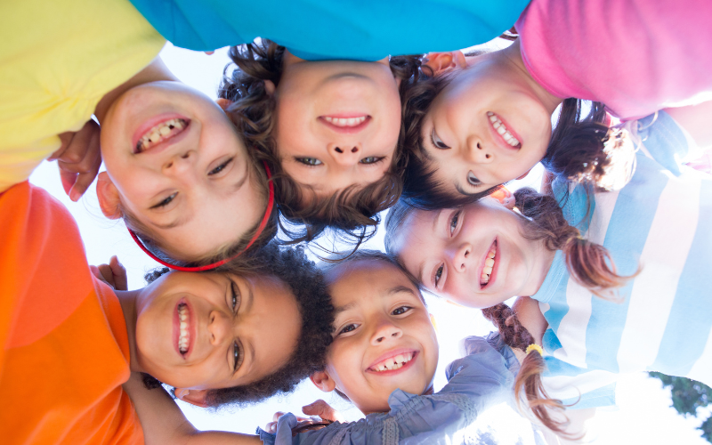 Six children standing in a circle with their heads together looking down at the camera below.