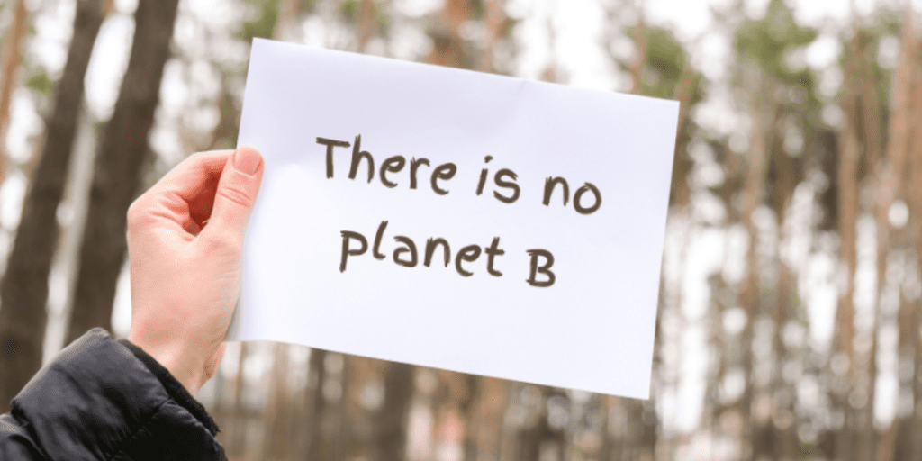 A hand holds a sign with the text "There is no planet B" against a background of blurred trees.