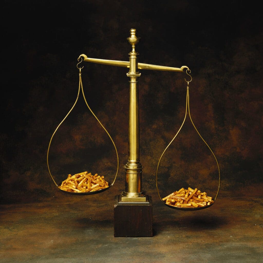A vintage balance scale is depicted with an equal amount of golden fries on both sides against a dark brown background in the image titled _getty-images-1xIW0FpLDmw-unsplash_. The crispy fries fill the hanging bowls, symbolizing balance and equity, much like the delicate climate we strive to maintain.