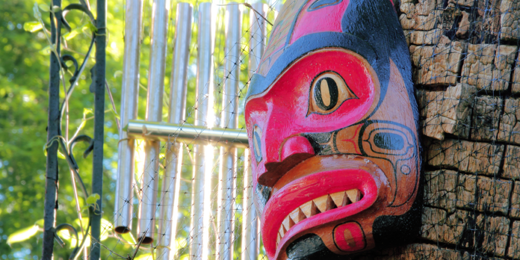 A colorful, carved Indigenous mask hangs on a tree.